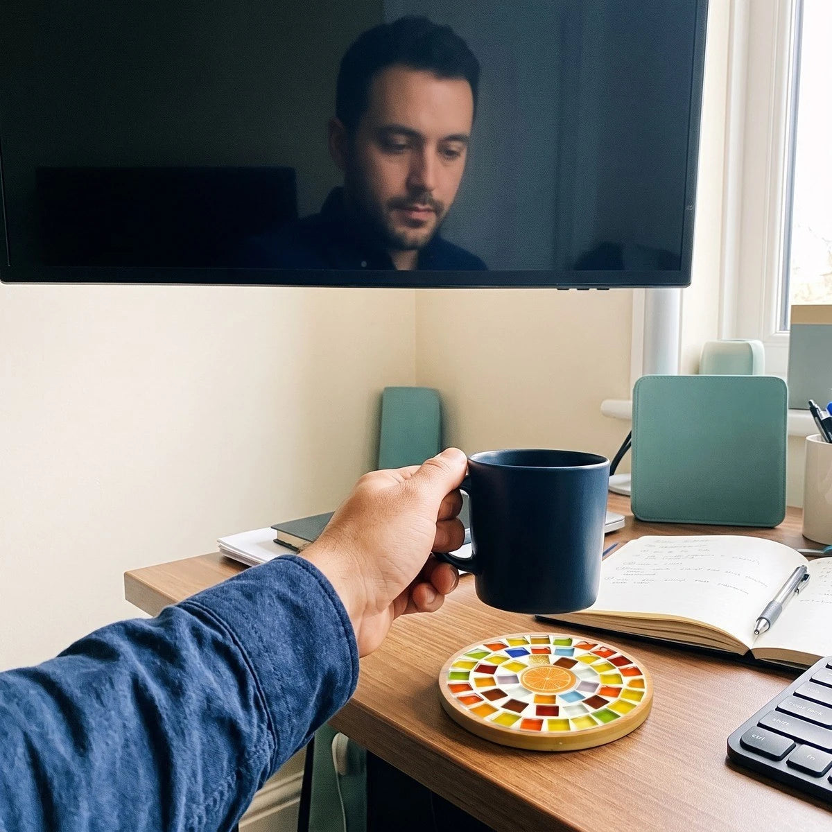 Adult maker Jamie R. with a mosaic coaster and coffee at a home desk