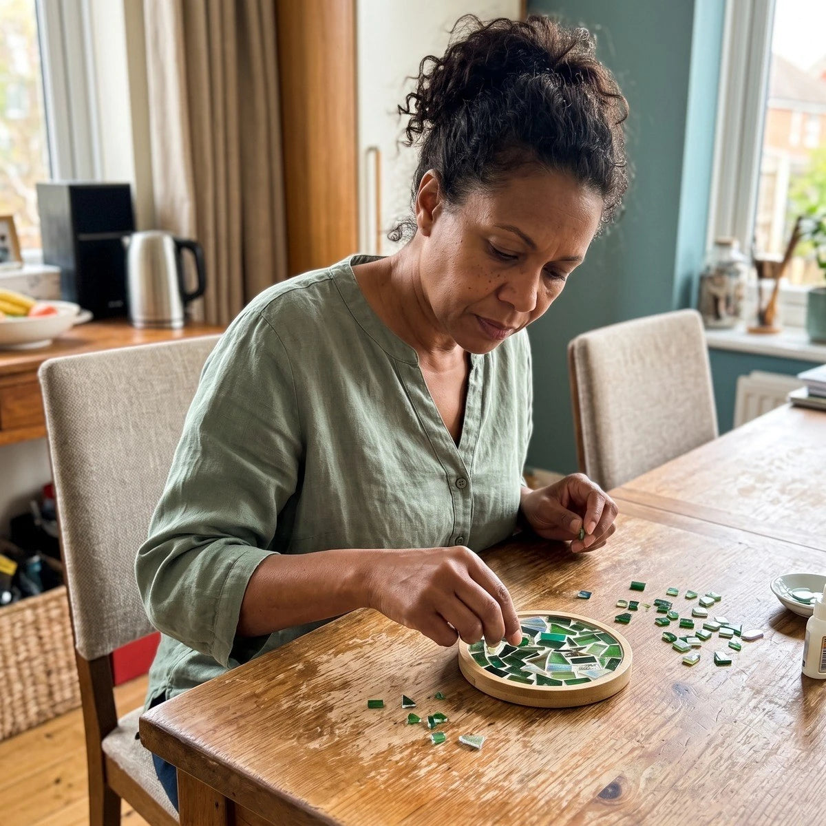 Adult maker Kelly L. arranging glass pieces at a sunny dining table